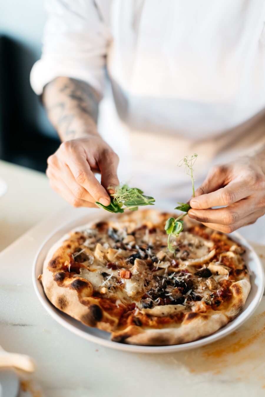 Bilden visar en person som dekorerar en pizza. Pizzaugn, elektrisk variant är ett väldigt bra val för att snabbt komma igång med pizzautbudet i din restaurang.